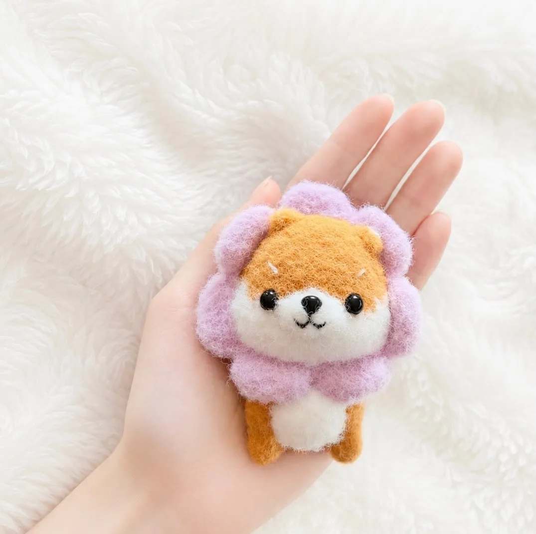 Tan and white crochet dog framed by lilac petals, held over a white blanket