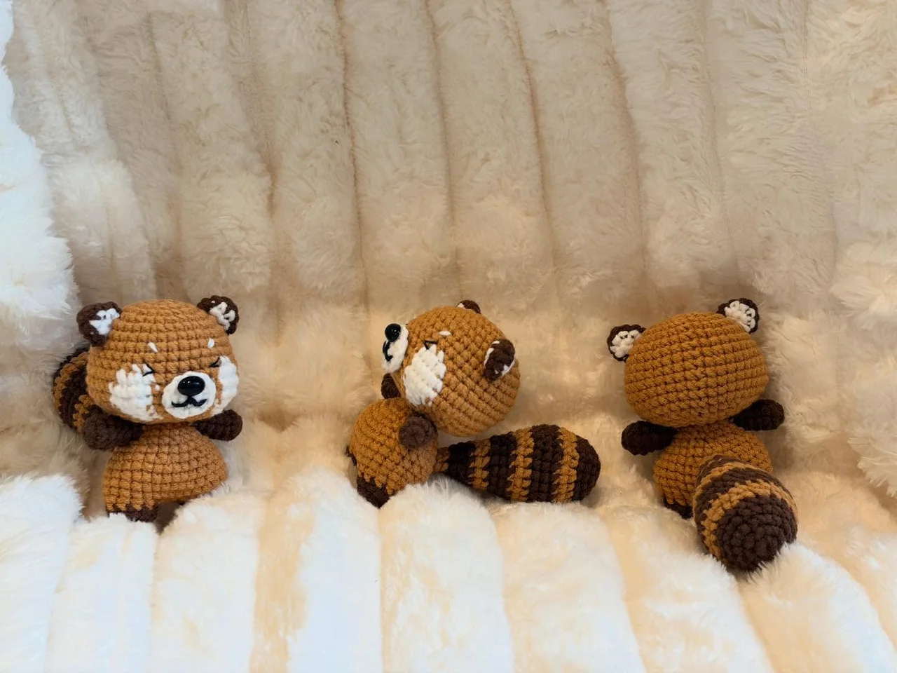 Brown crochet red pandas showing cream face markings and long striped tails on a white blanket