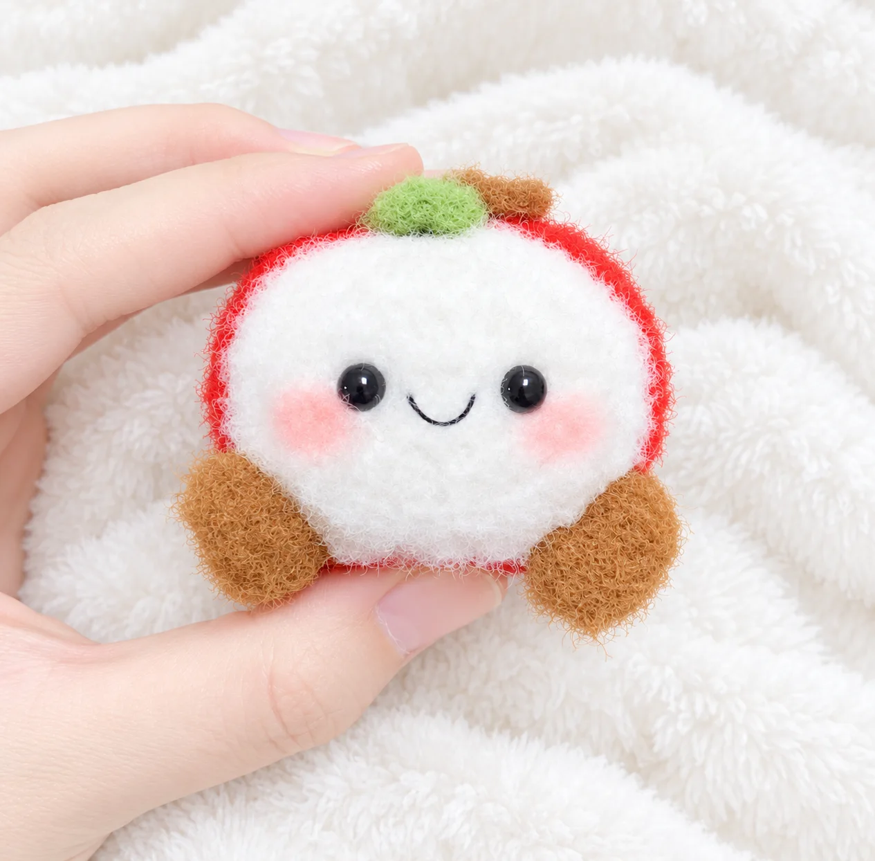 Fluffy red Christmas apple with a smiling cream face, rosy cheeks, a green leaf, a brown stem and brown feet, held in a hand