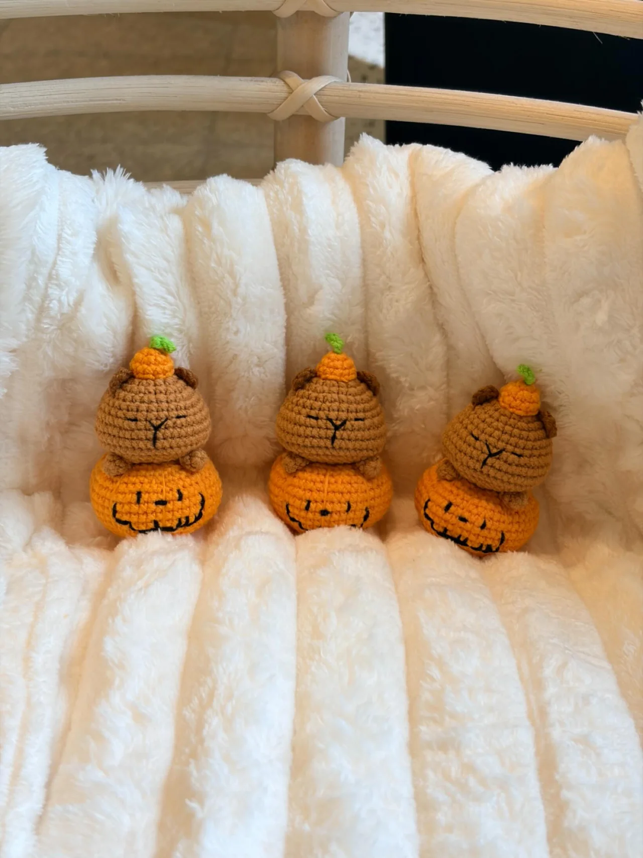 Three little crochet animals in orange pumpkin costumes and tiny pumpkin hats, sitting on a white blanket