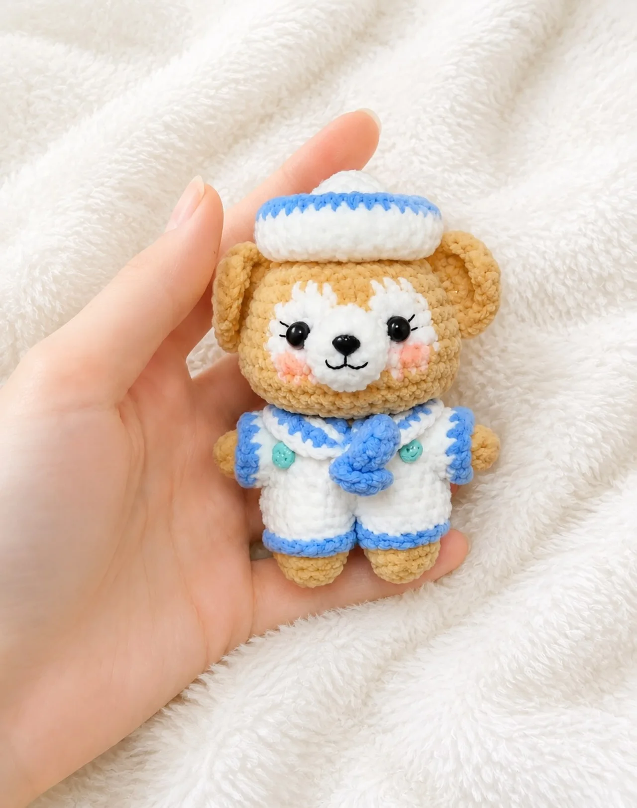 Golden crochet dog in a white and blue sailor outfit and matching hat, held over a white blanket