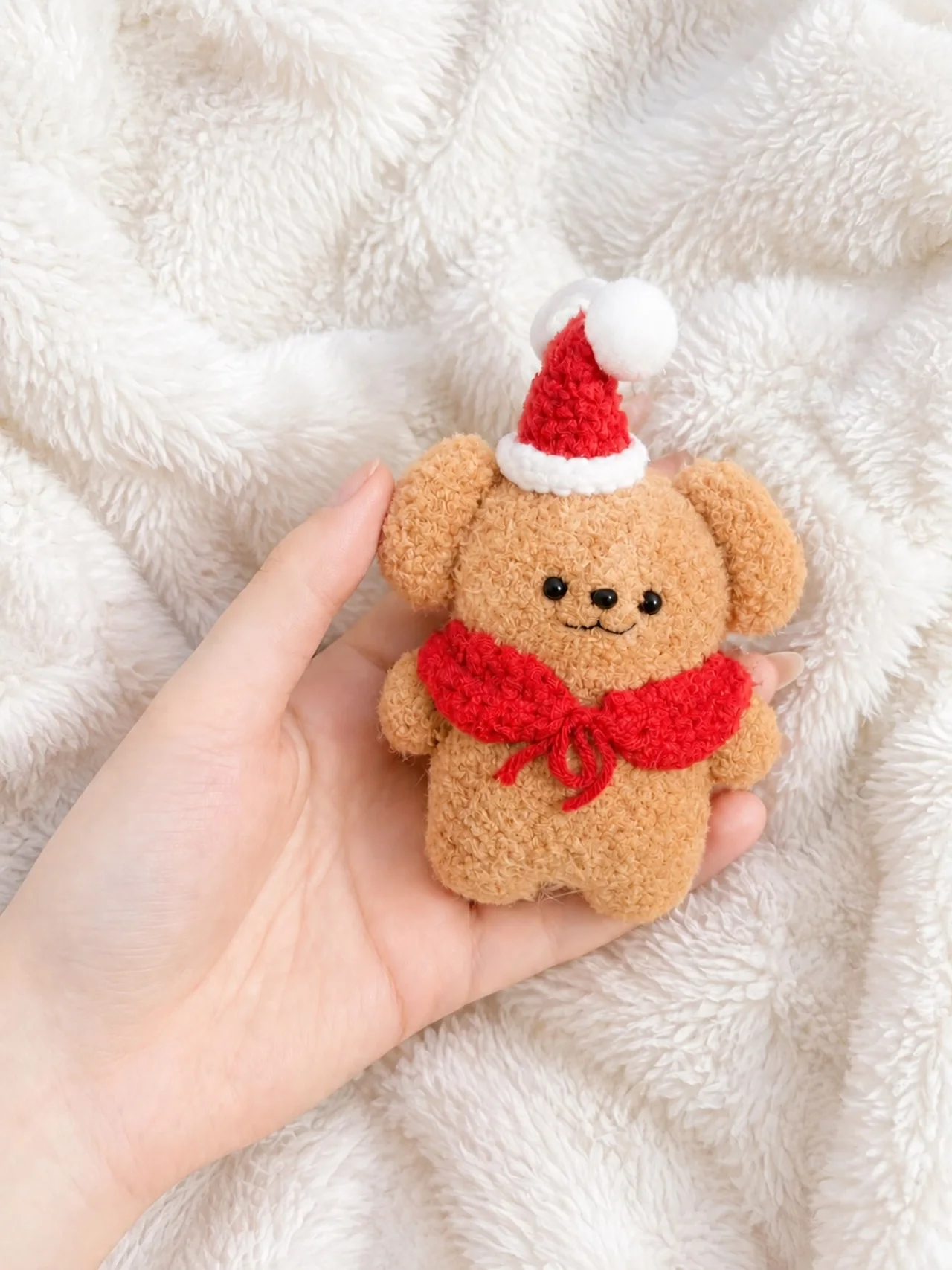 Golden crochet bear wearing a red Santa hat and red collar, held over a white blanket