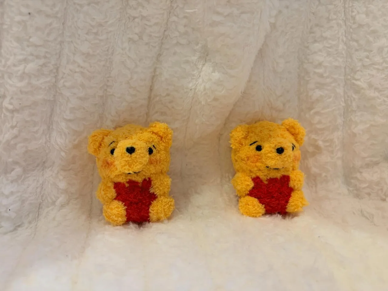 Two golden crochet bears in red tops, sitting together against a white blanket
